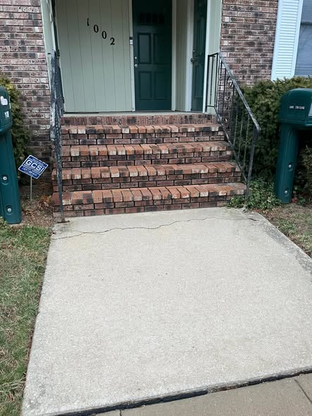 Front entrance with weathered brick steps and a cracked concrete slab before replacement